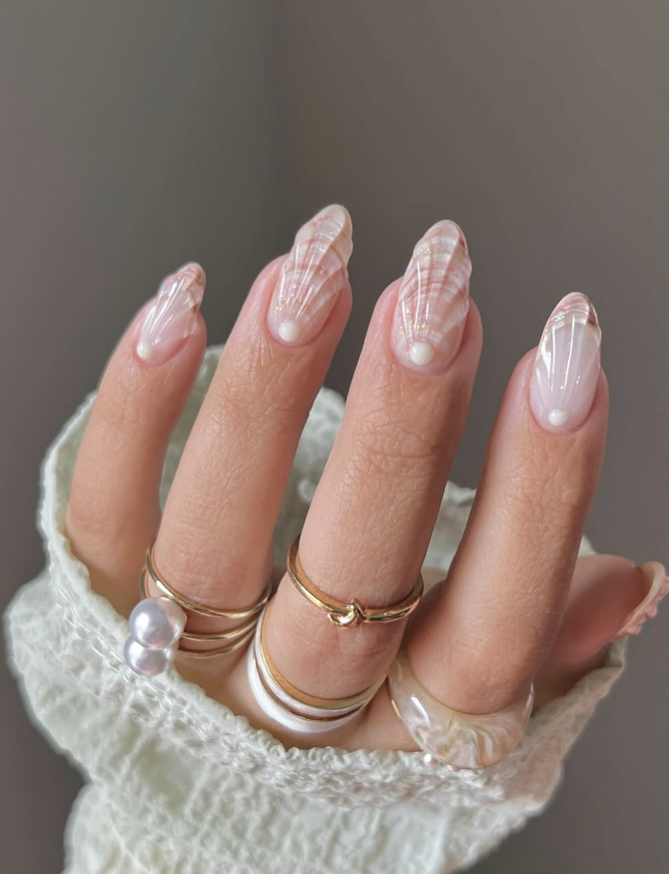 Long oval nails featuring a 3D sculpted iridescent seashell texture and tiny pearl embellishments at the base, highlighting cute June nail ideas.