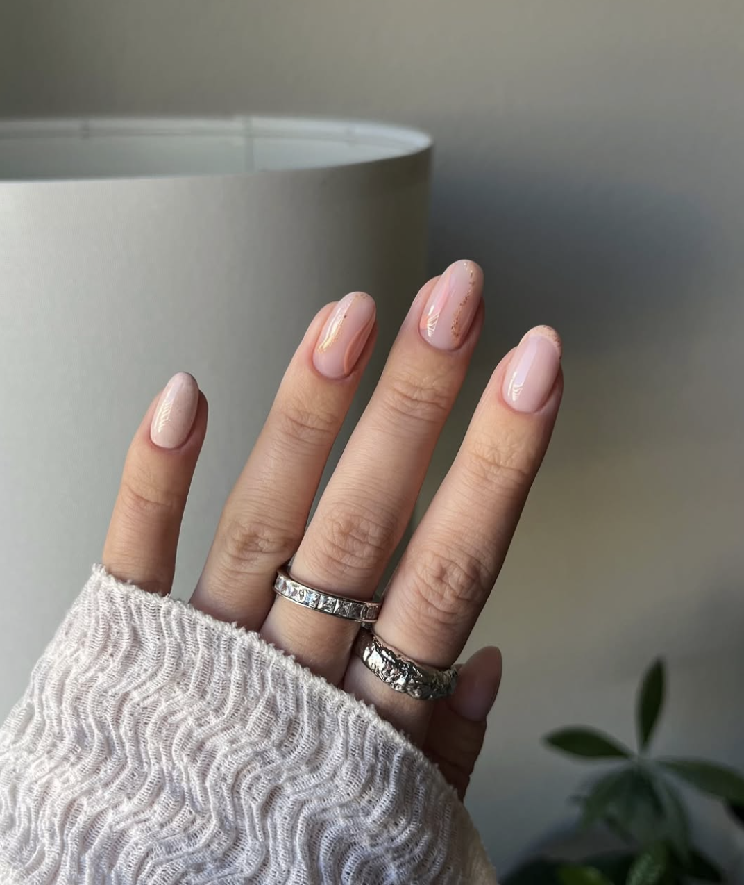 A close-up of a hand with short almond-shaped natural nails featuring a sheer rosy pink base and organic gold foil accents along the edges and tips.