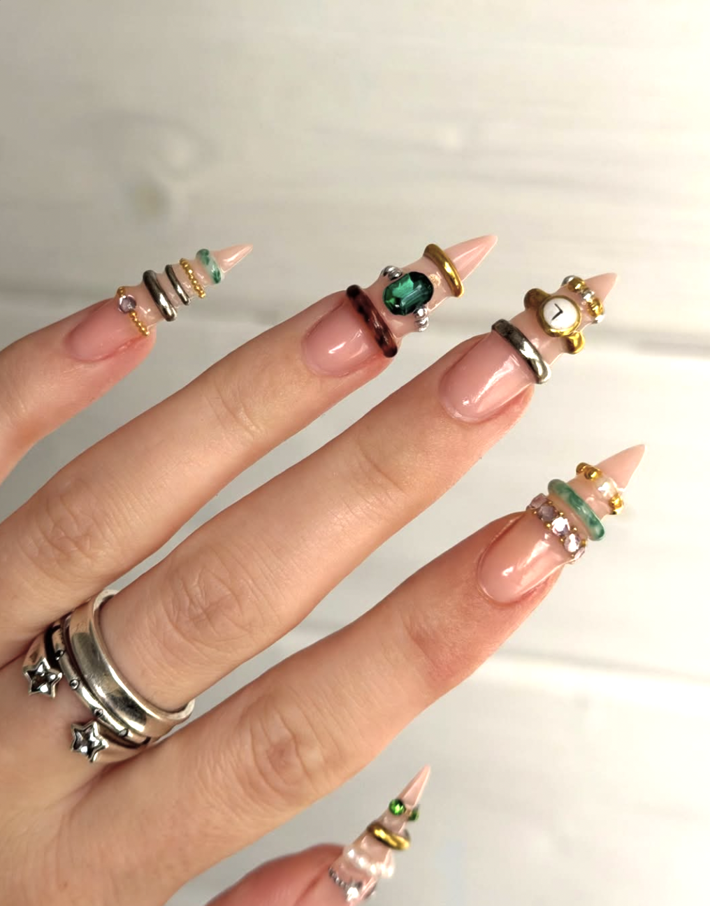 Long tapered nude nails featuring thick 3D gold bands, hanging star charms, and a signature pierced nail tip.