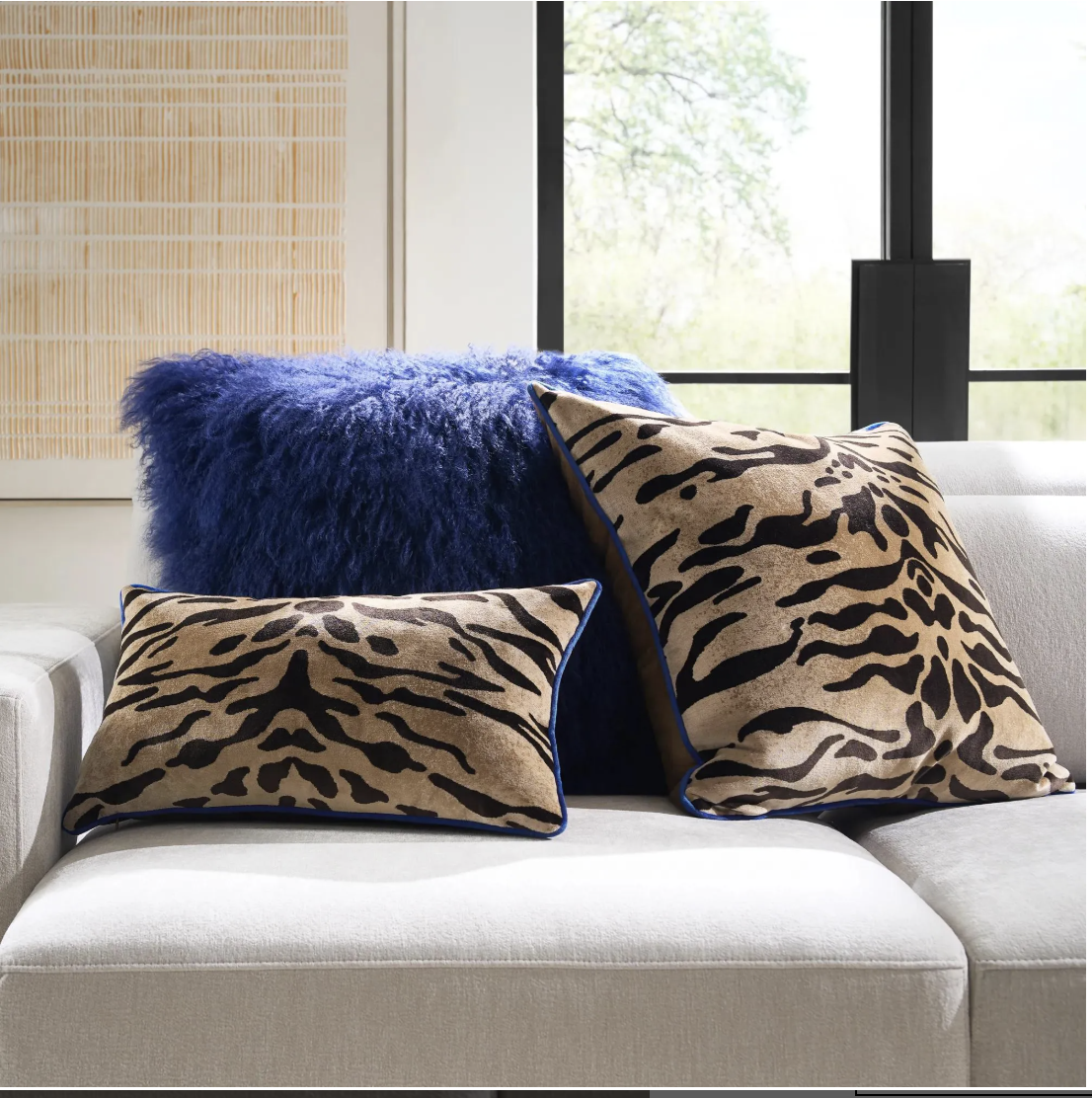 A neutral beige sofa styled with luxurious textured throw pillows, including a tiger stripe pattern pillow and a plush cobalt blue velvet accent pillow.