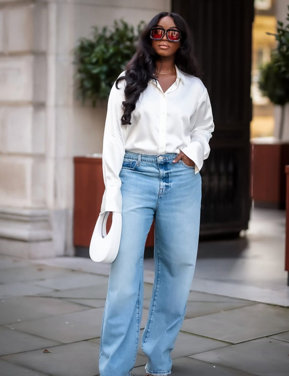 A woman wearing an oversized white button-down shirt with light wash baggy jeans and a white crescent bag, styled for an everyday casual look.