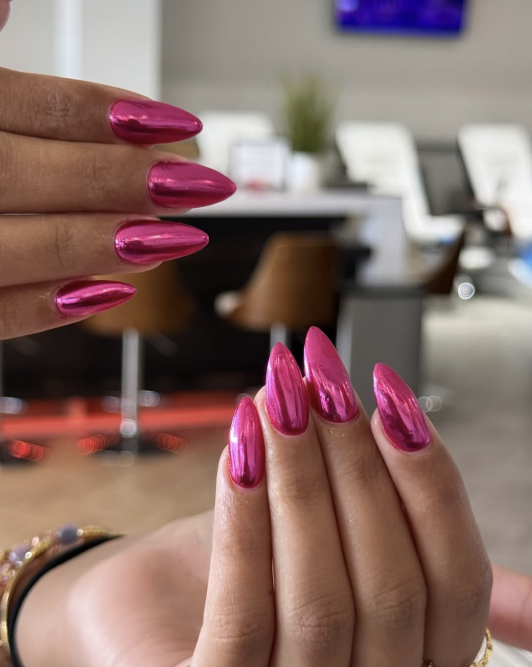 A close-up of long almond-shaped nails with a vibrant magenta pink mirror chrome finish.