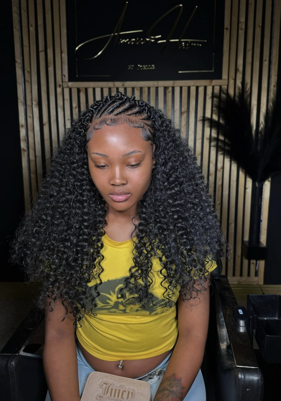 A woman with neat flat twists along the scalp that transition into long, voluminous curly extensions, featuring a clean center part and detailed edges.