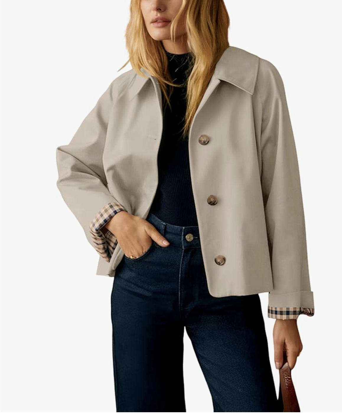 A woman styling a cropped beige short trench jacket from Amazon over a black turtleneck and dark wash straight-leg jeans, part of a spring capsule wardrobe for women in their 60s.