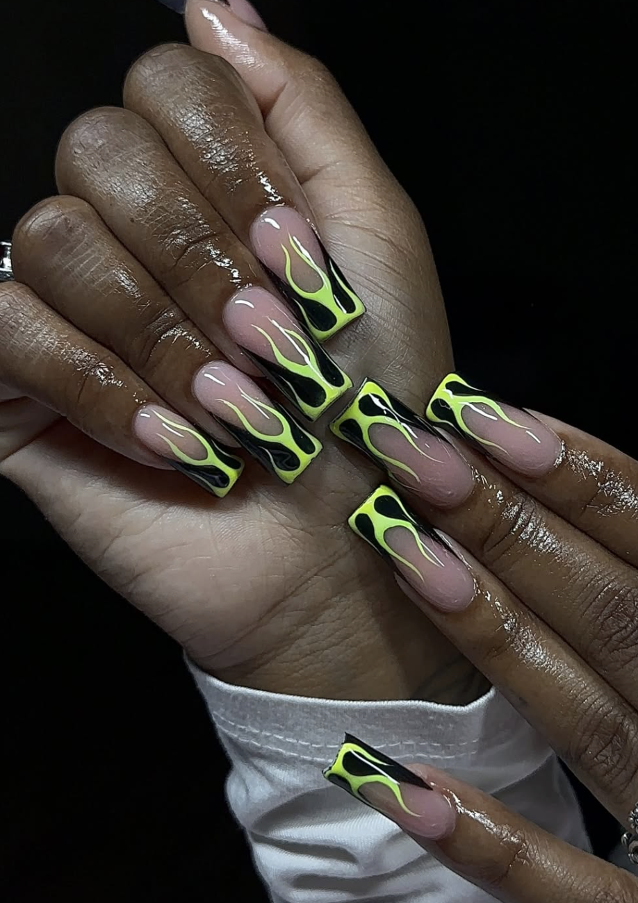 Extra-long square nails with a sheer nude base and vibrant neon green flame designs outlined in black, mimicking a French tip shape.