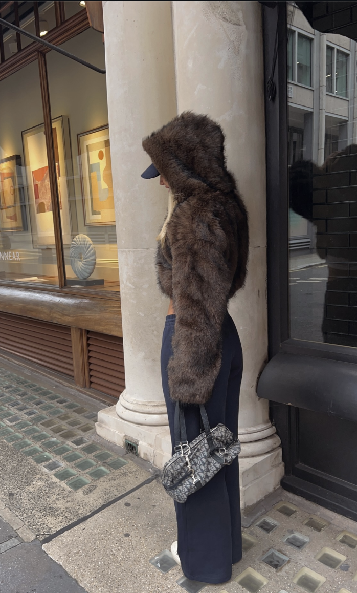 Cropped brown textured jacket and gray top with wide navy trousers, a cap, light sneakers and a small dark bag.