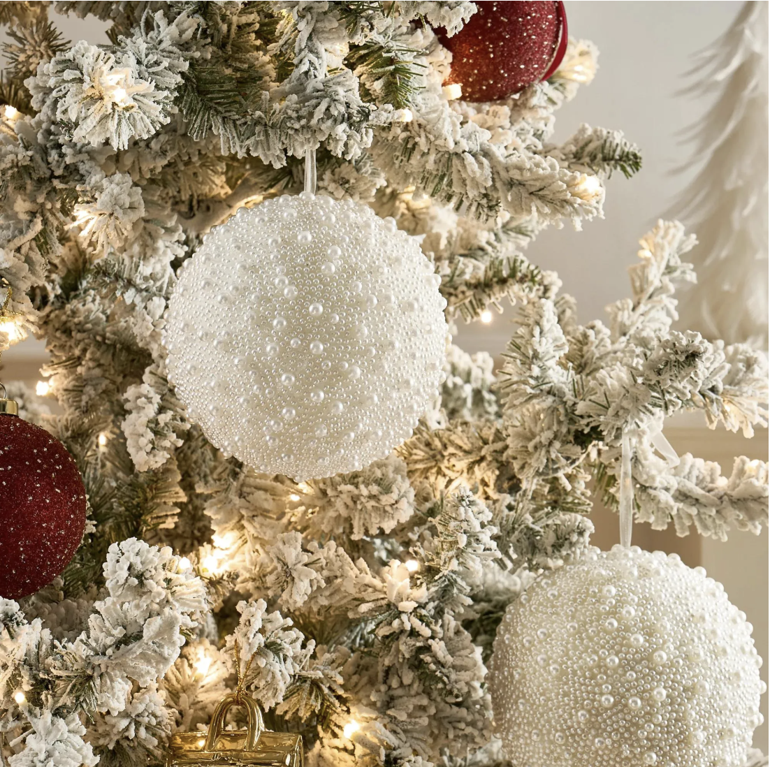 Ivory pearl-beaded ball ornaments and burgundy glitter ornaments on a flocked Christmas tree with warm white lights.