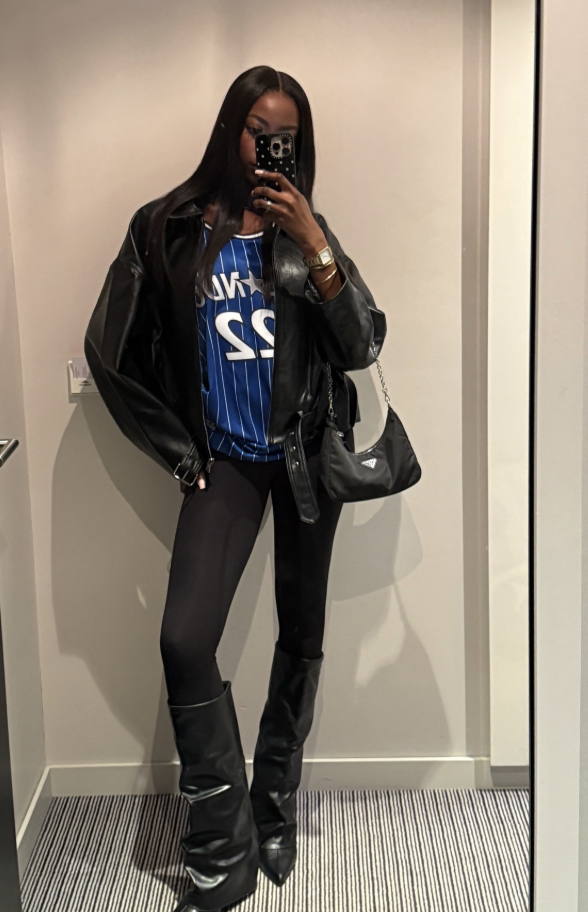 Woman at an NBA game wearing an Orlando jersey under a black leather jacket with dark jeans.