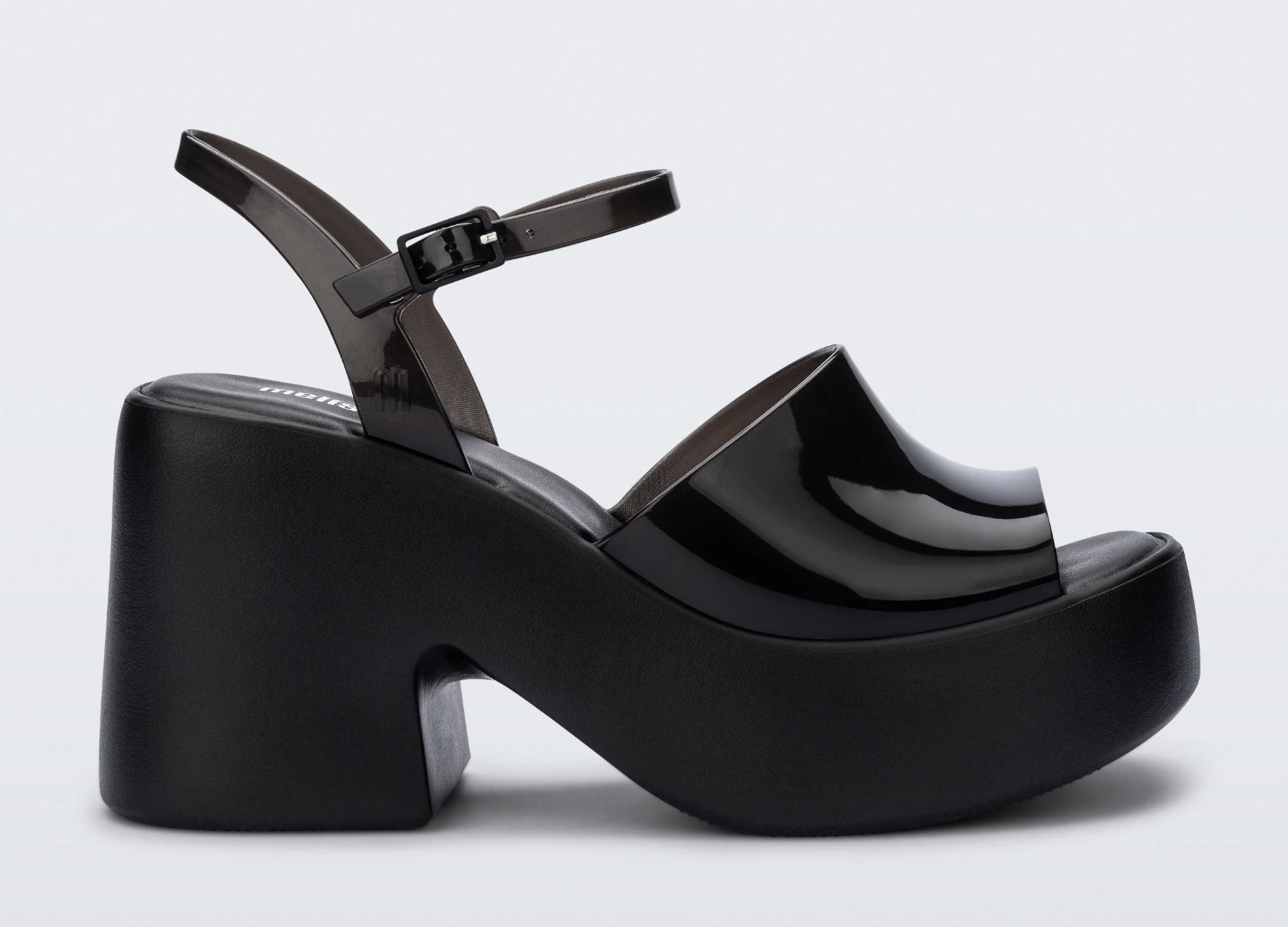 A close-up product view of a chunky black patent jelly platform sandal featuring a thick block heel, a wide front toe strap, and an adjustable ankle strap with a buckle.