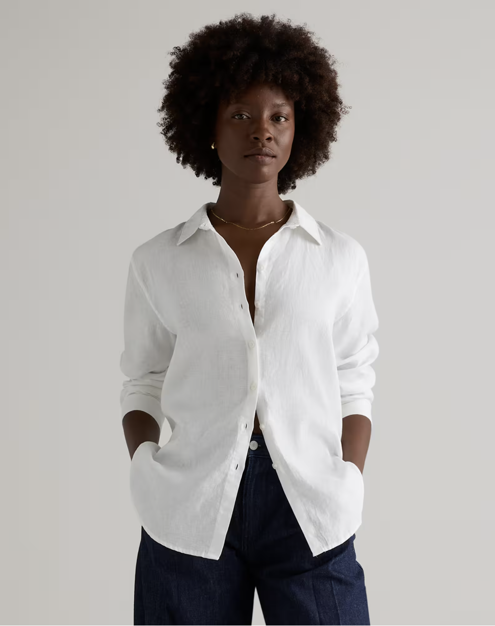 A woman wearing an oversized white linen button-down shirt from Quince tucked into dark wash jeans, showing a classic everyday outfit idea.