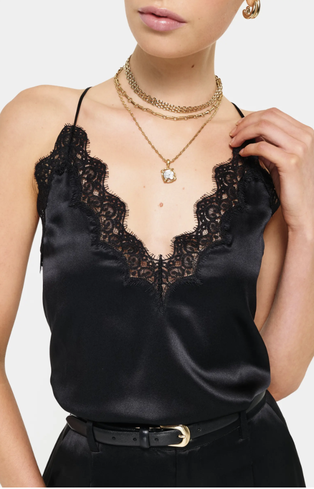 A person wearing a black satin camisole with a delicate black lace trim along the V-neckline, tucked into black trousers with a gold buckle belt.