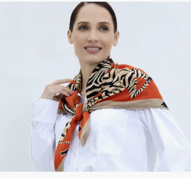 A woman wearing a white button-up shirt with the Youzey Kensington Scarf, featuring an orange border and a black and white tiger stripe pattern, tied around her neck.