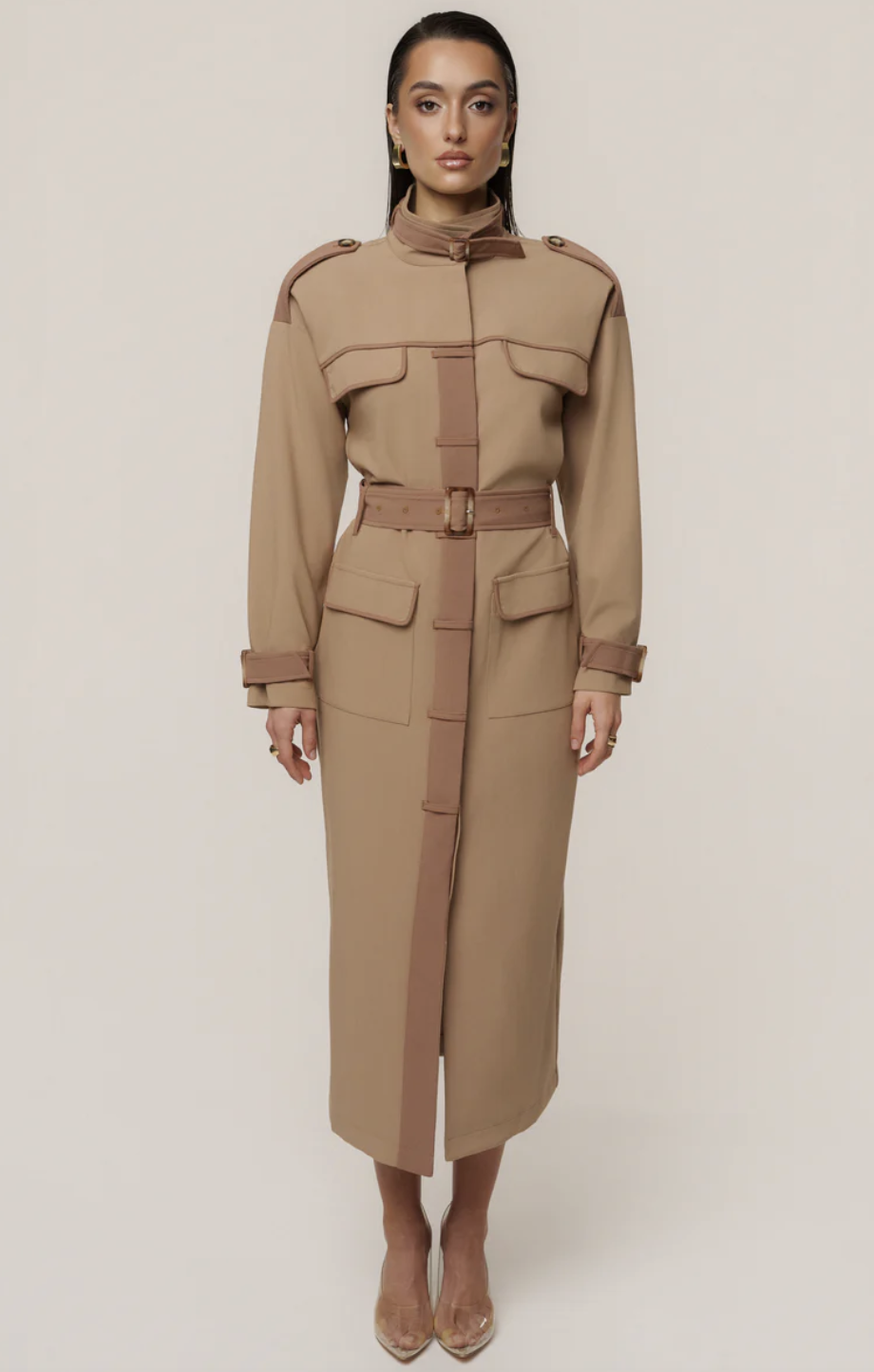 A woman wearing a structured, tan belted midi dress with a high collar and trench-coat inspired lapels and pockets.