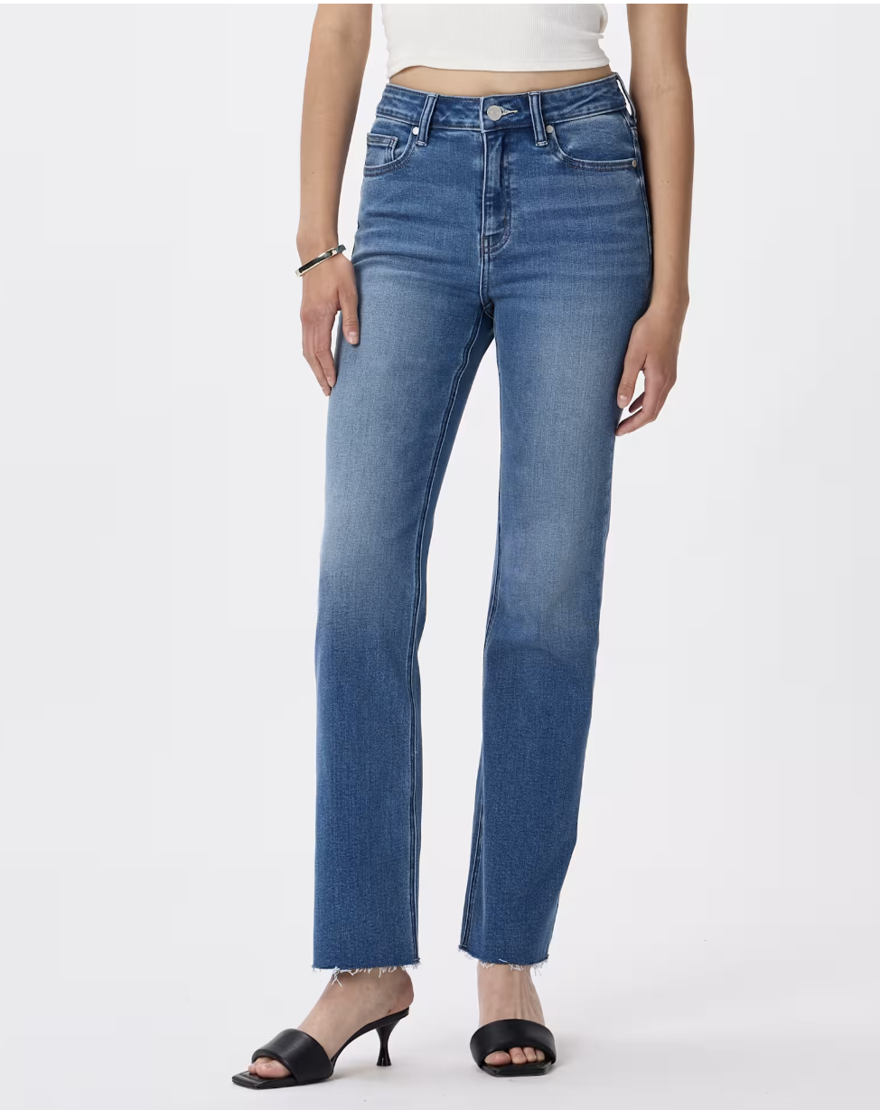 A person wearing NYDJ Bella Stretch Straight Jeans in a medium wash with a raw hem, paired with black square-toe heeled sandals.