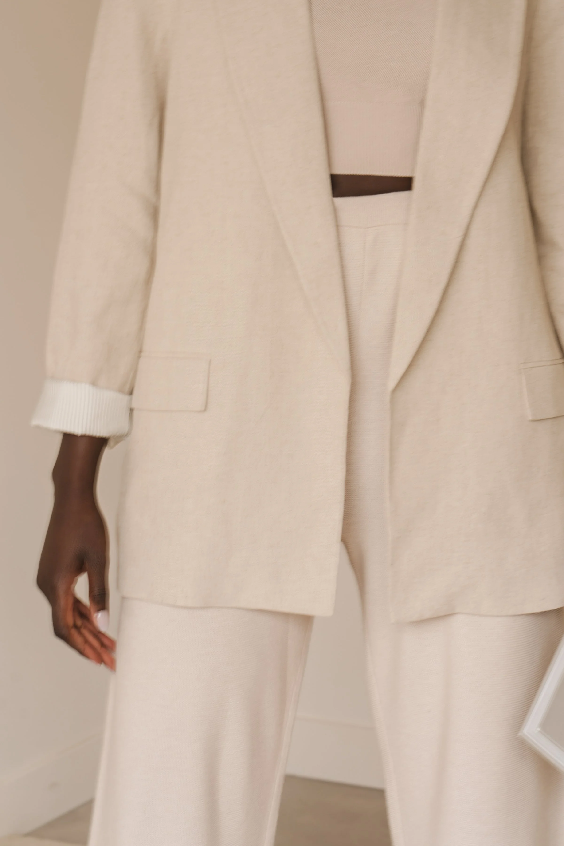 A person wearing a beige oversized blazer and matching trousers with their hand hanging down, against a plain background.