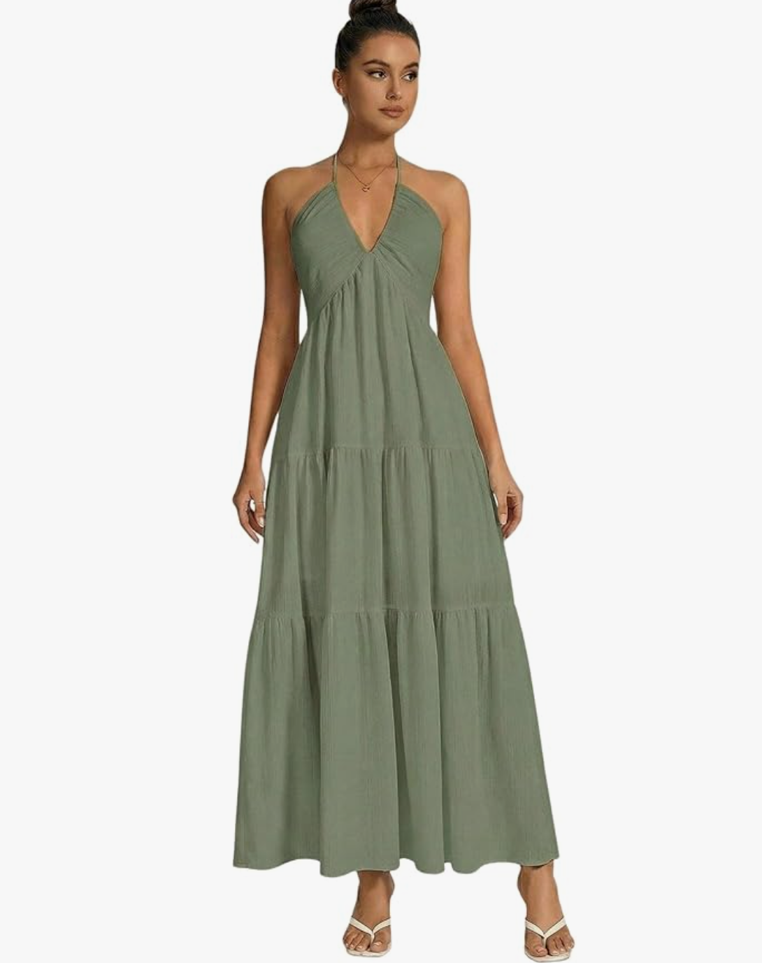 A front view of a woman modeling a sage green cotton halter maxi dress, featuring a deep V-neckline, a tiered skirt silhouette, and an open back design.