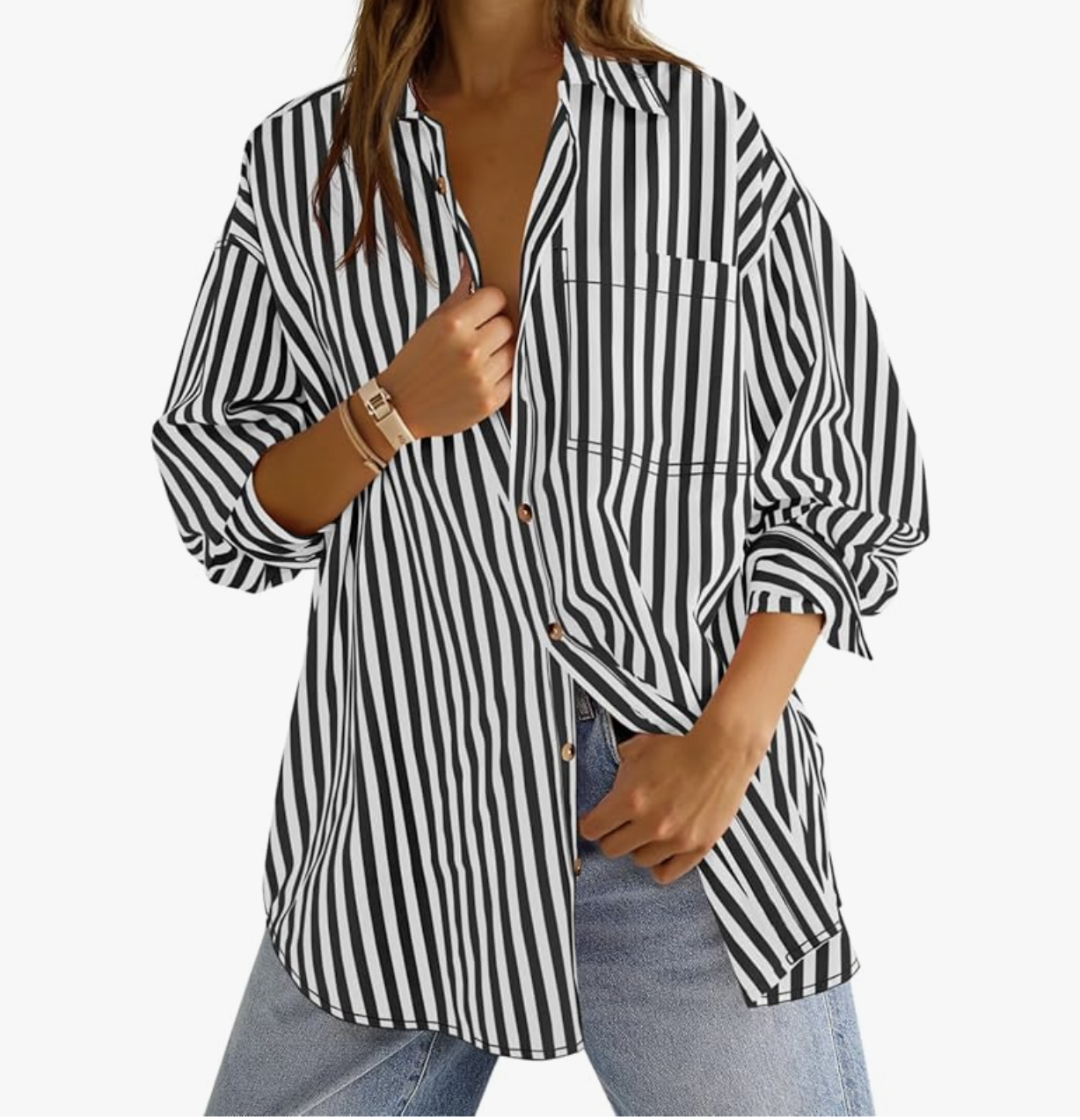 A close-up of a woman wearing a relaxed black and white vertically striped button-down shirt with long sleeves, styled with thin gold bracelets and a classic watch.