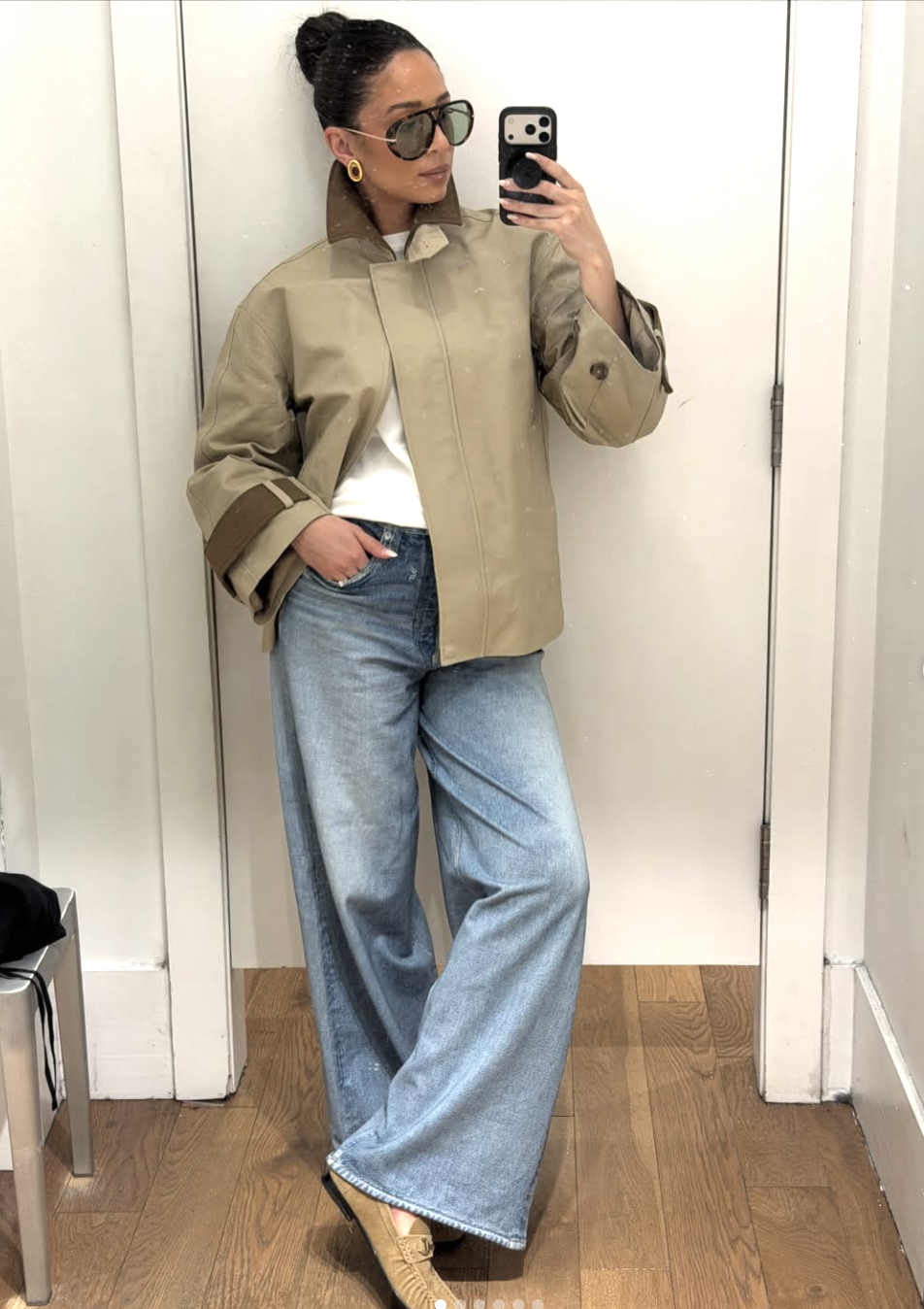 A woman wearing a tan cropped double-breasted trench coat paired with high-waisted denim to visually shorten a long torso and elongate the leg line.