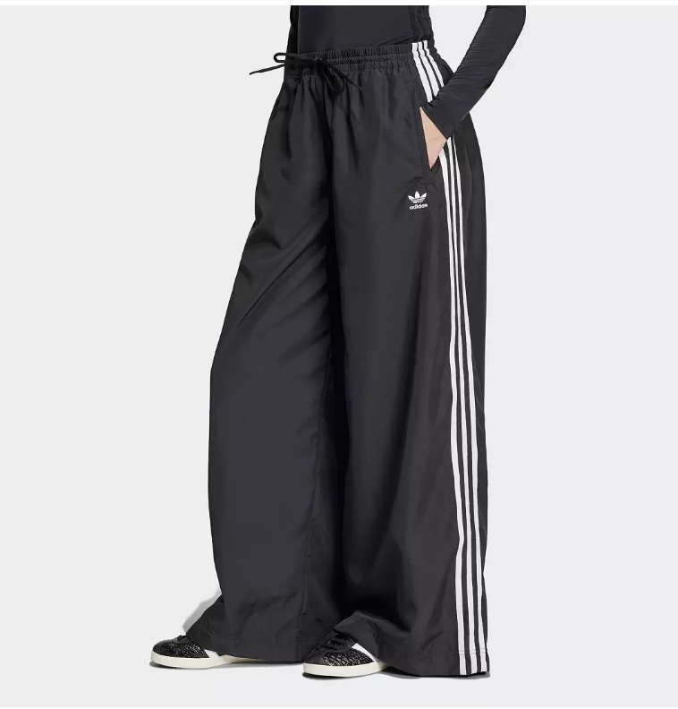 Close-up detail of the black [adidas Originals Adilenium Trackpants](https://go.shopmy.us/p-45396786) showing the high-waisted drawstring fit, embroidered Trefoil logo, and iconic white stripes for a clean minimalist look.