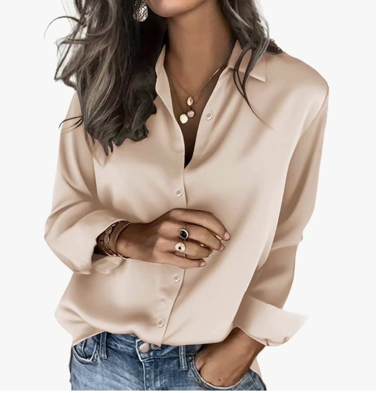 A woman wearing a champagne-colored silk button-down shirt tucked into jeans, accessorized with gold layered necklaces and rings.