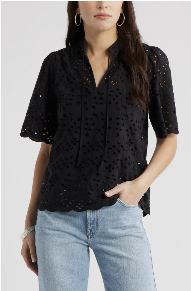 A woman wearing a black eyelet split-neck cotton blouse with short flutter sleeves, styled with light-wash denim jeans for a business casual capsule wardrobe.