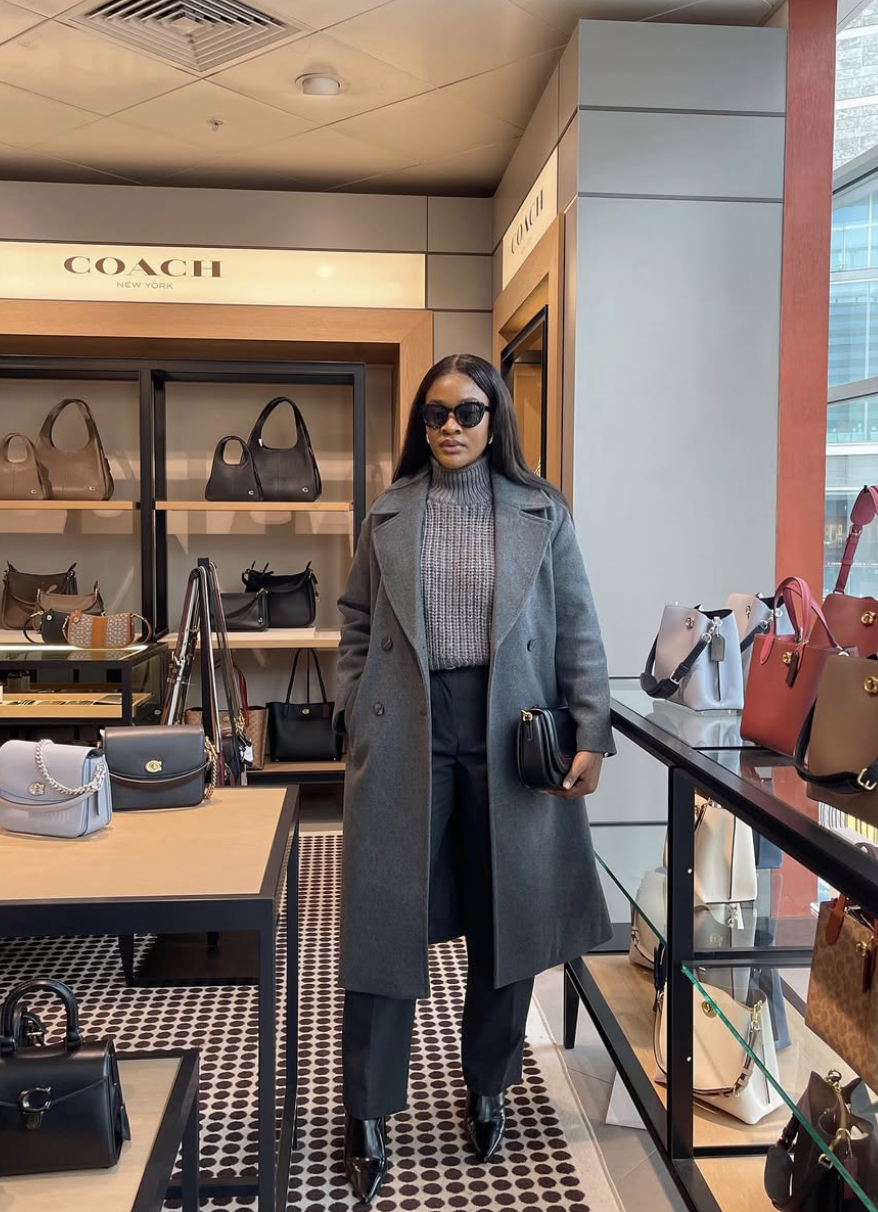 A fashion editor-approved winter outfit featuring dark cropped pants paired with sleek, black pointed-toe ankle boots and a long grey coat, demonstrating how a slim boot shaft creates a clean line at the ankle.