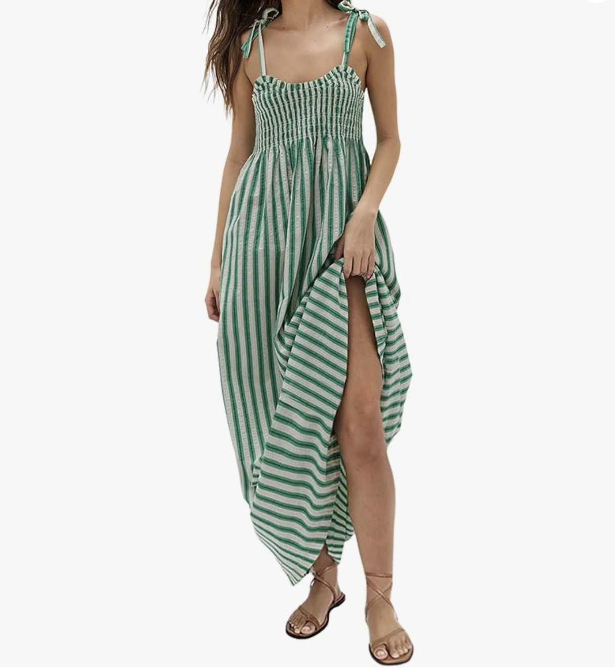 A full-length view of a woman wearing a green and white vertically striped strapless maxi dress with a smocked bodice and a high thigh-slit, paired with tan strappy flat sandals.