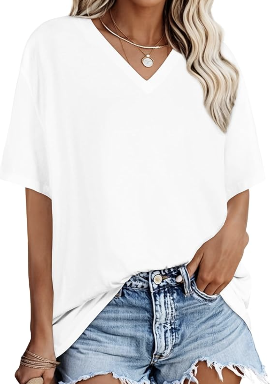 A close-up of a woman wearing a loose-fitting white V-neck t-shirt tucked into light-wash denim jeans, accessorized with layered gold necklaces.