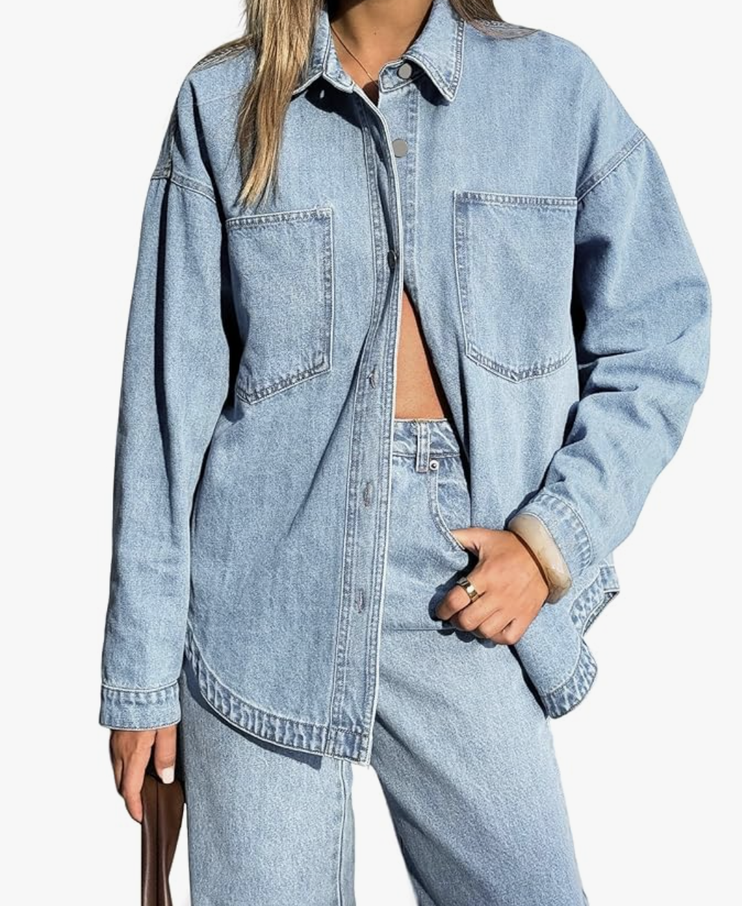 A woman wearing an oversized light blue denim button-down shirt tucked into matching light wash jeans.