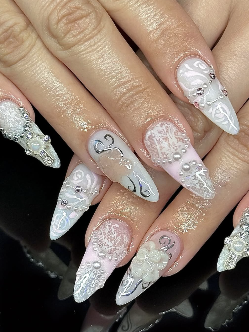 Long almond-shaped acrylic nails with a nude base and intricate white hand-painted lace patterns.