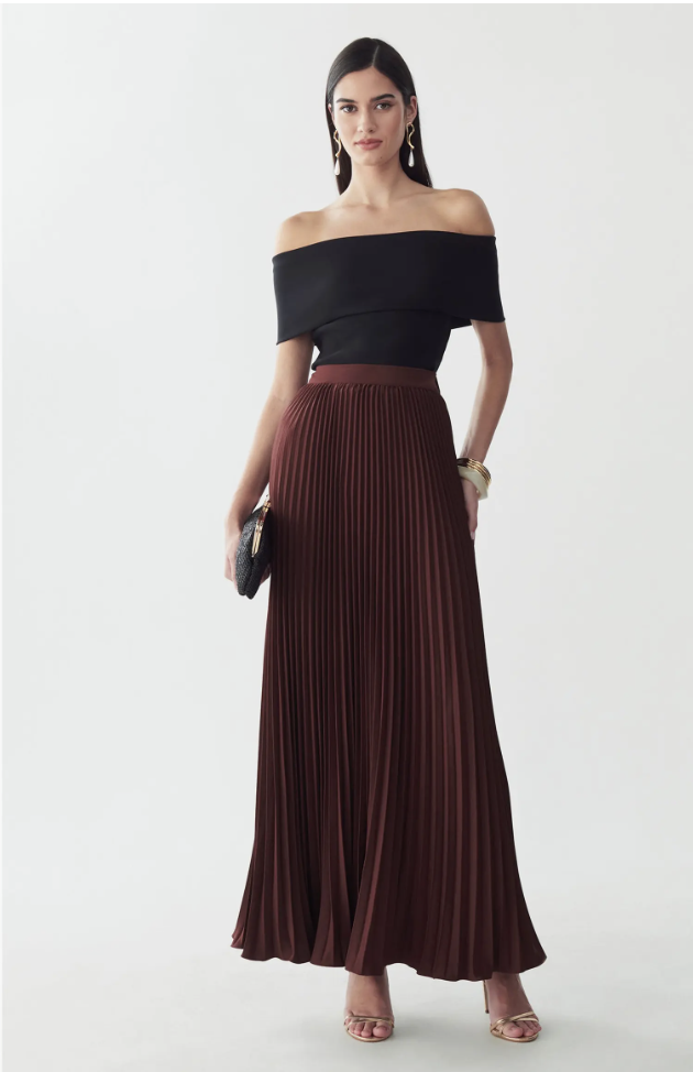 Woman wearing an off-the-shoulder black top paired with the Willa Amur burgundy pleated midi skirt and strappy metallic heels