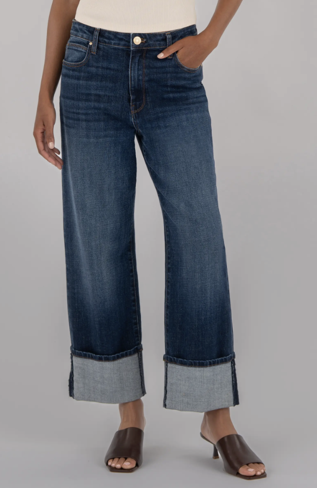 A woman wearing dark wash wide-leg jeans by KUT from the Kloth, featuring a thick cuffed hem and styled with dark brown pointed-toe mules.