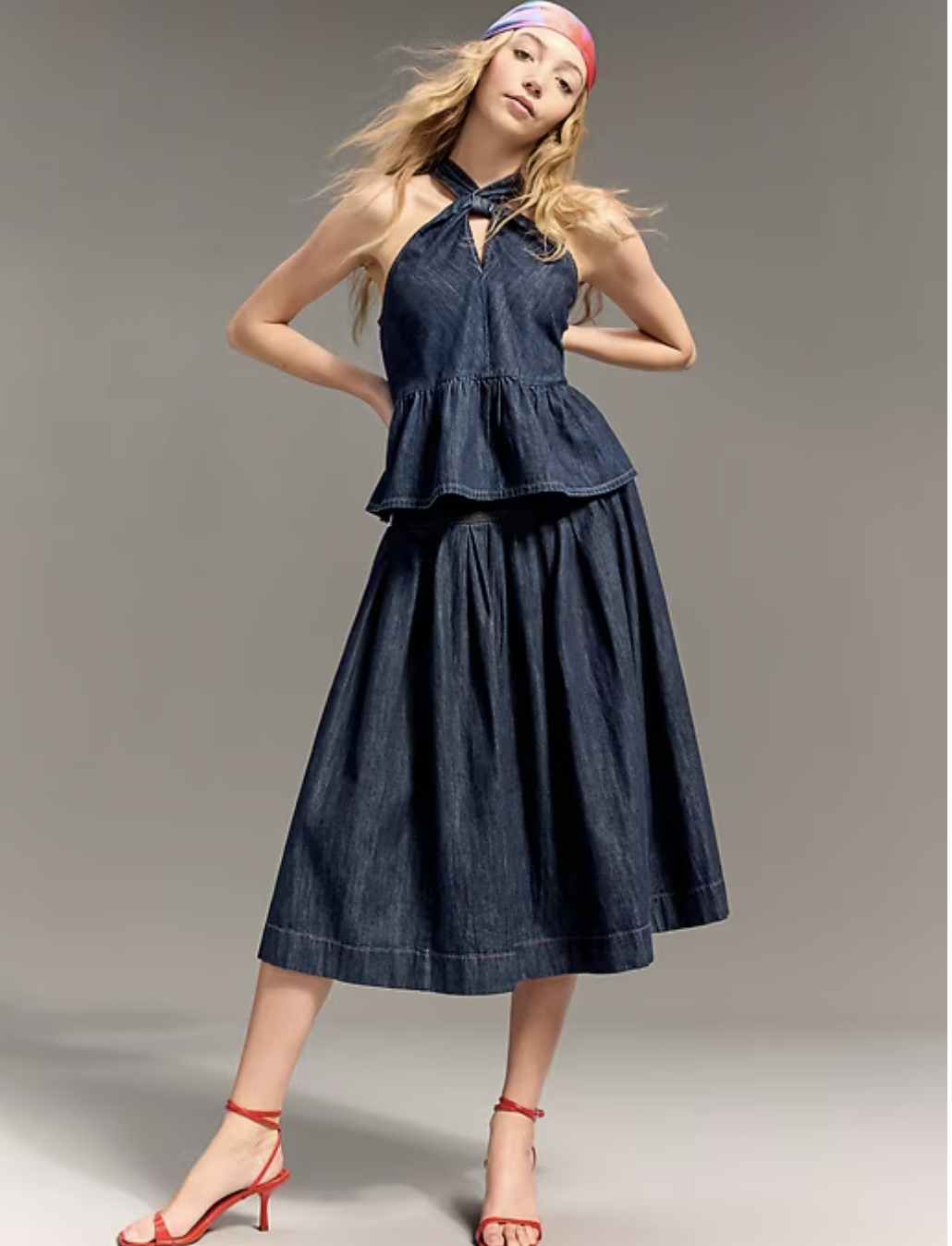 Model wearing the Old Navy x Christopher John Rogers dark wash denim twisted halter peplum top and matching midi skirt with red heels and a colorful headscarf.