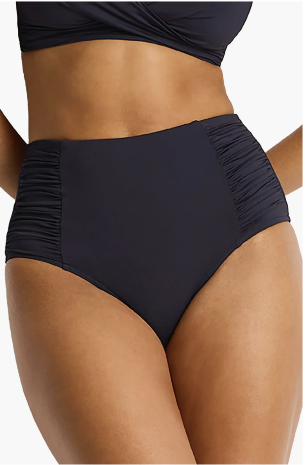 A woman modeling the Sea Level High Waist Gathered Side Swim Bottoms in "Night Sky" navy blue, featuring rippled side ruching and a flattering high-rise fit.