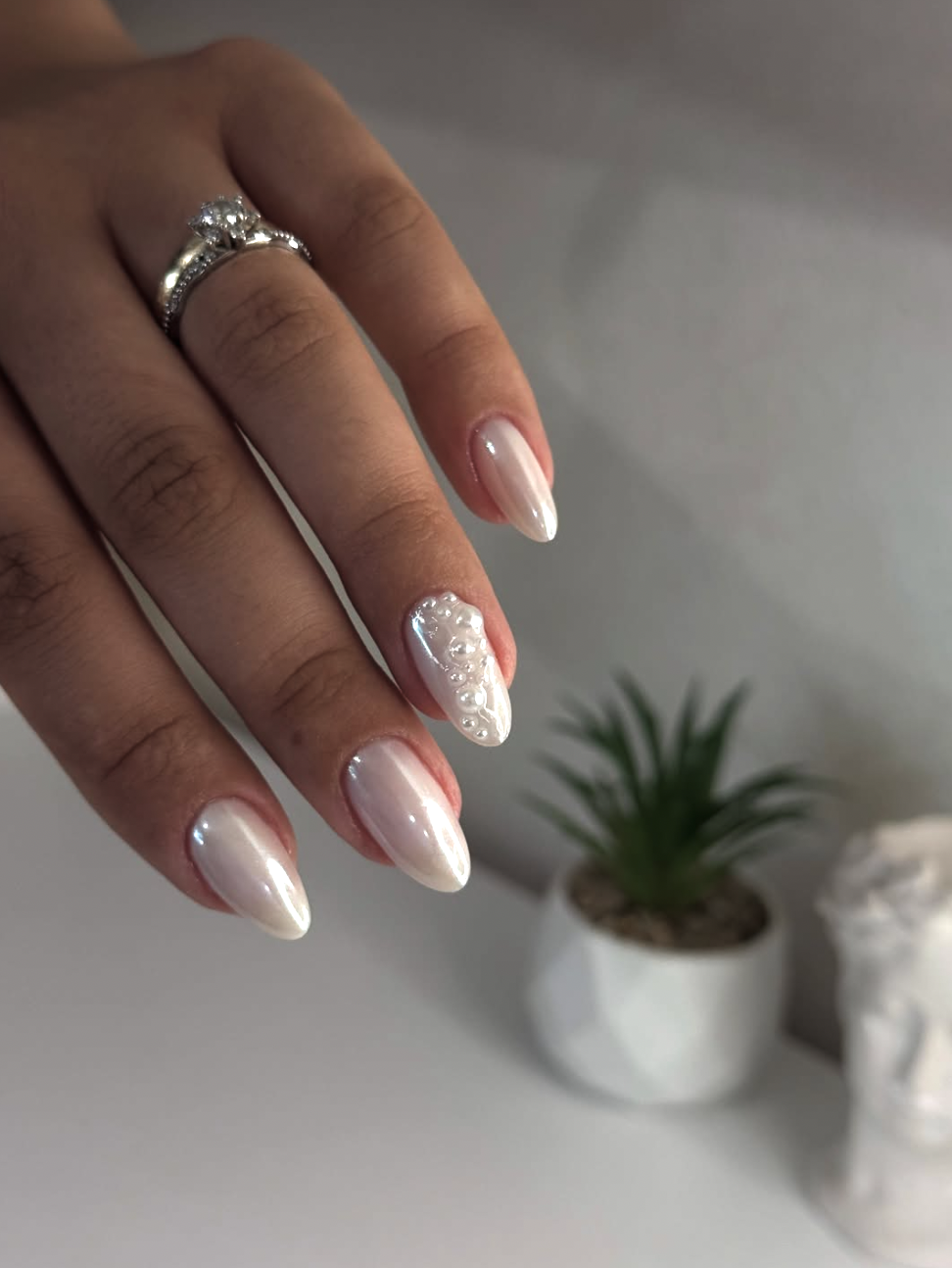 Long almond-shaped nails with a glowing pearlescent chrome base, decorated with clustered pearl embellishments on the accent nail, highlighting cute June nail ideas.