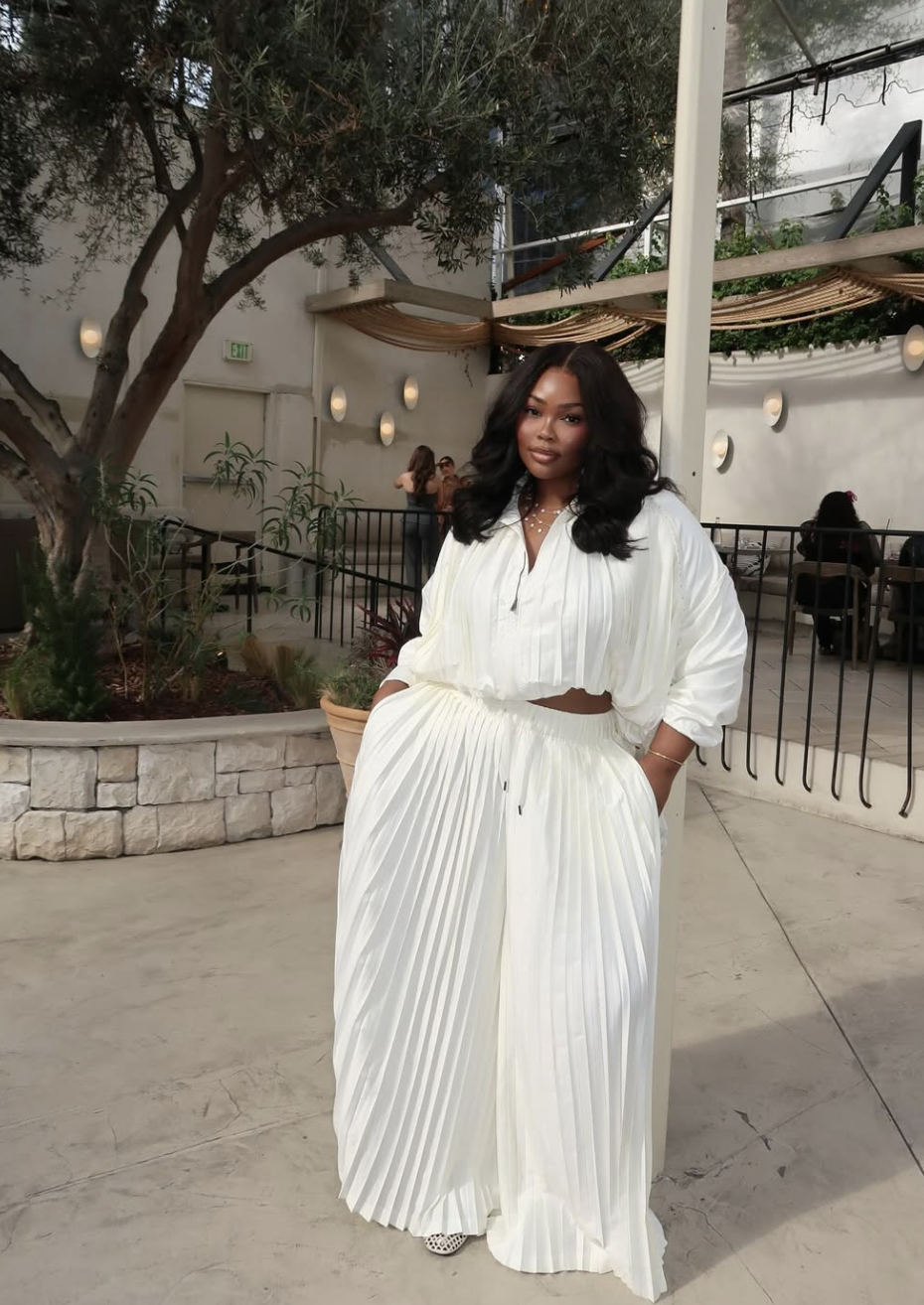 A woman wearing an elevated monochromatic white outfit featuring a cropped button-down shirt and high-waisted pleated wide-leg trousers.