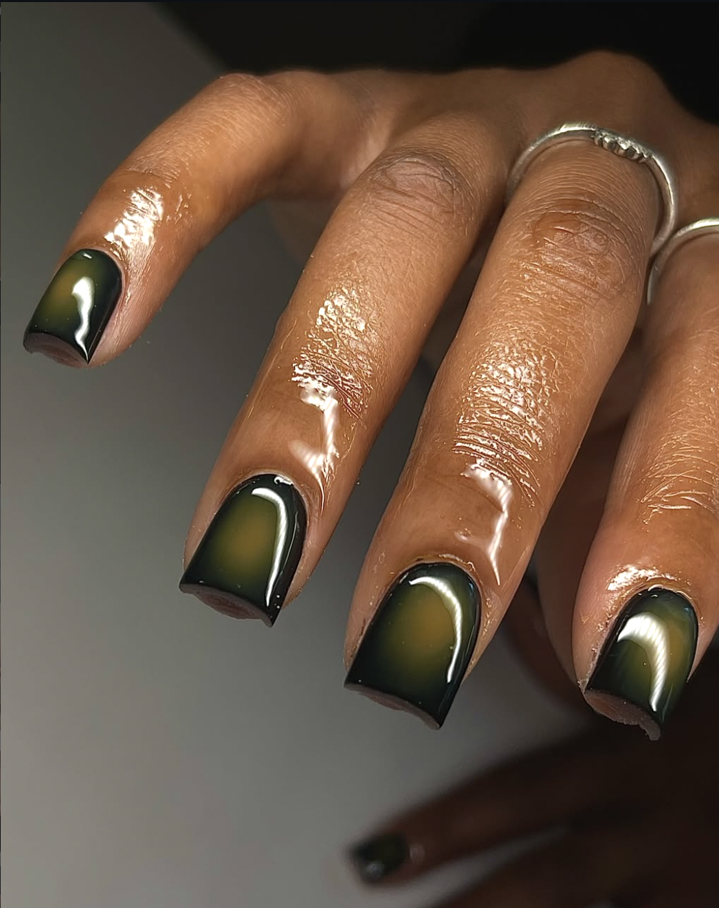 Close-up of short, square-oval nails featuring a glossy dark smoked olive green manicure.