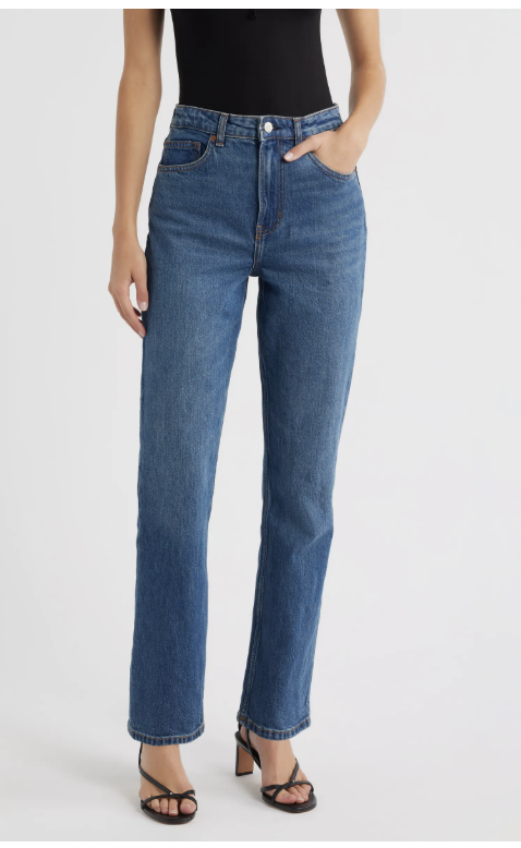 A close-up of a person wearing Reformation Jax Super High Waist Straight Leg Jeans in a medium-wash denim, styled with black strappy heeled sandals.