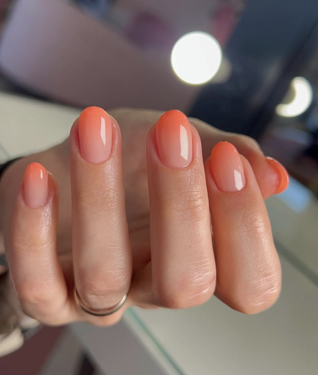 Long, almond-shaped nails showcasing a vibrant coral and peach ombre gradient finish, topped with a luminous pearl chrome glaze.