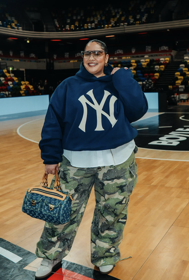 Woman wearing an oversized sporty knit with baggy gray jeans and a small structured handbag at a basketball game.