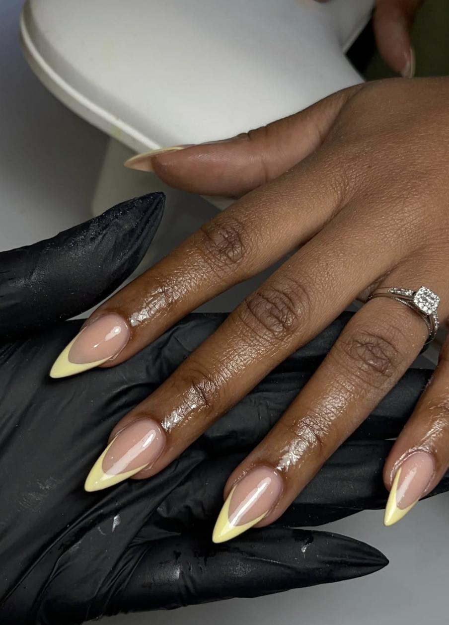 A close-up of a minimalist manicure featuring butter yellow French tips on long, almond-shaped nails, perfect for cute June nail ideas.