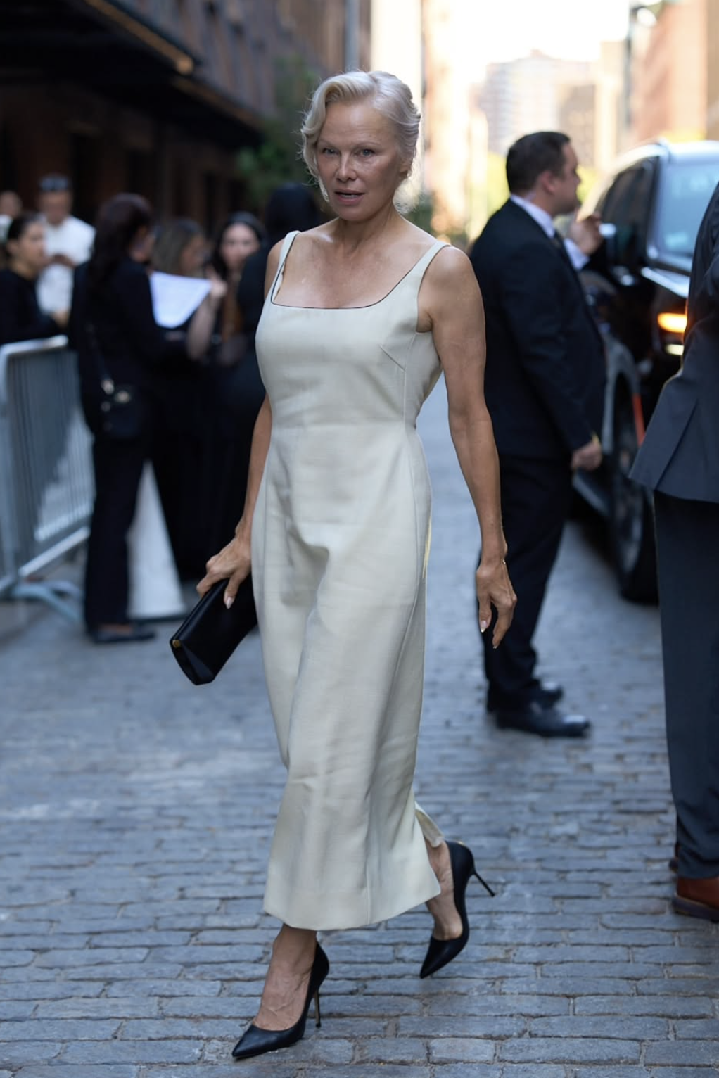 Pamela Anderson wearing a cream square-neck midi dress with black pointed pumps at the Calvin Klein fashion show.