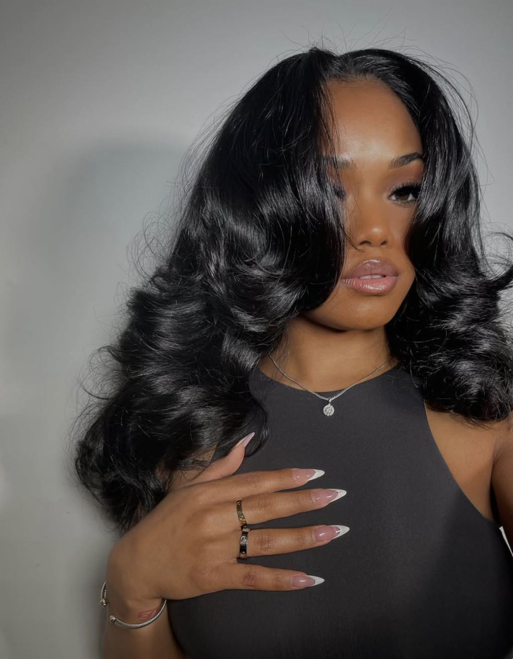 A woman with long, voluminous black waves and wide-sweeping curtain bangs, wearing a black top and a silver necklace, showcasing how bangs balance a diamond face shape.