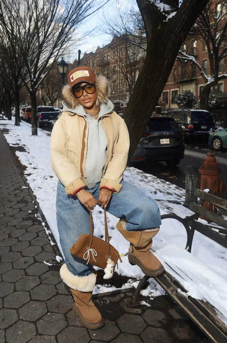 Cream shearling-style jacket over a gray hoodie, with blue jeans tucked into tall tan boots.