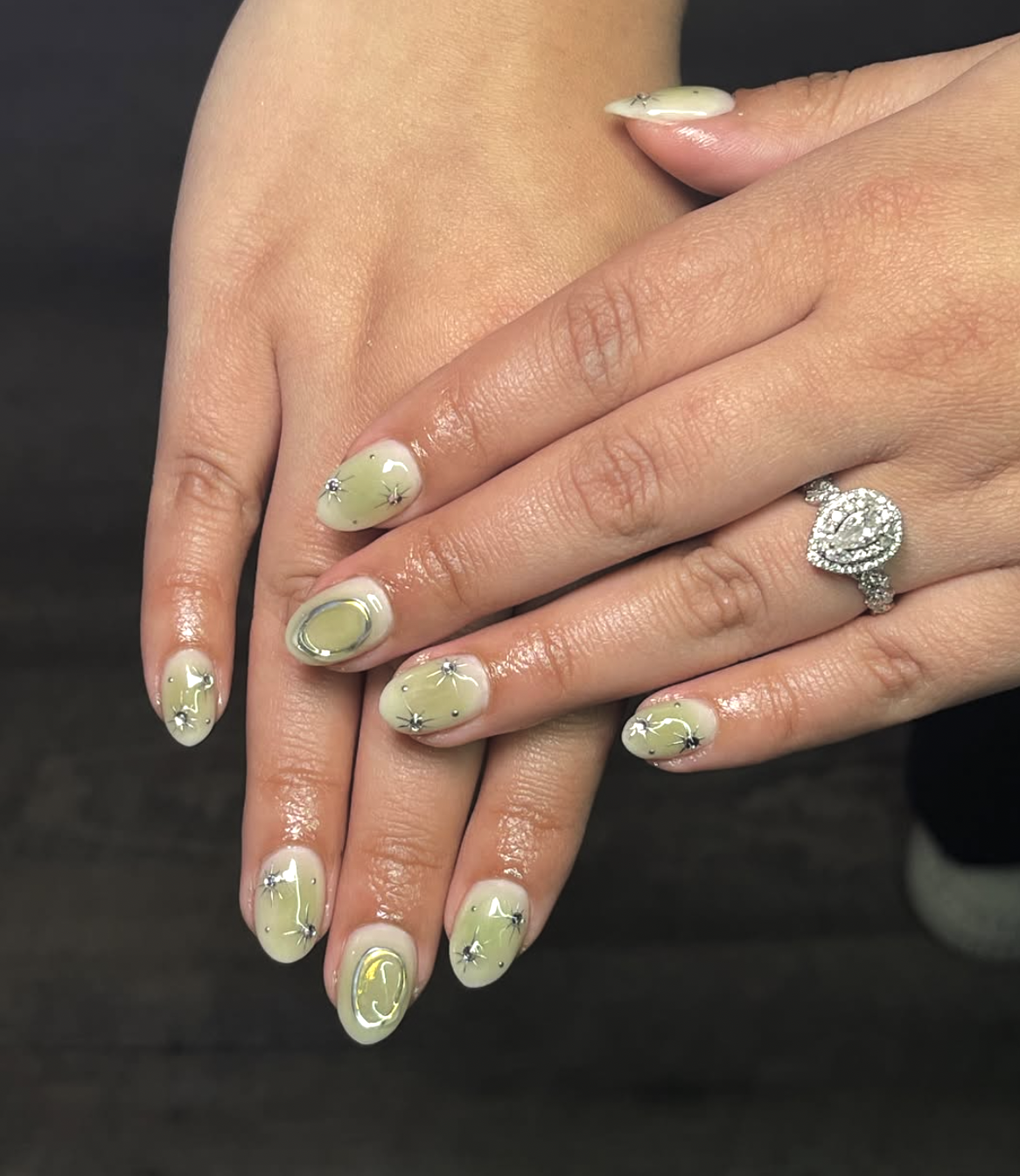 close-up of a matcha green nail art design featuring 3D silver metallic accents and textured patterns on almond-shaped nails."