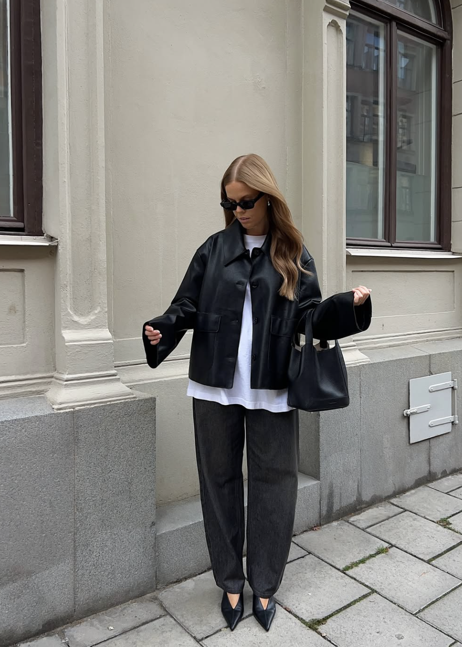 A woman wearing an oversized white graphic t-shirt with dark wash baggy jeans and black pointed-toe flats, representing a casual everyday outfit.