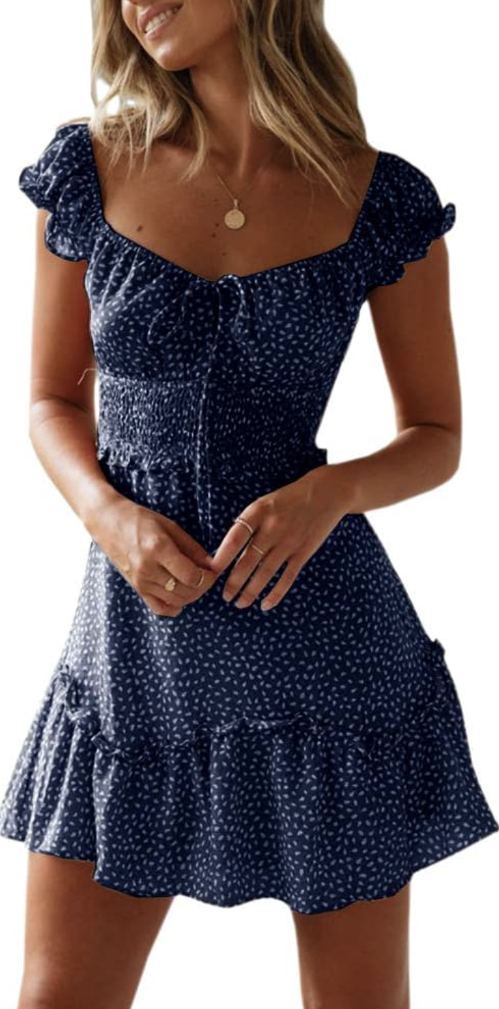 A woman wearing a navy blue mini dress with a white floral print, featuring a sweetheart neckline, ruffled cap sleeves, and a tiered skirt.