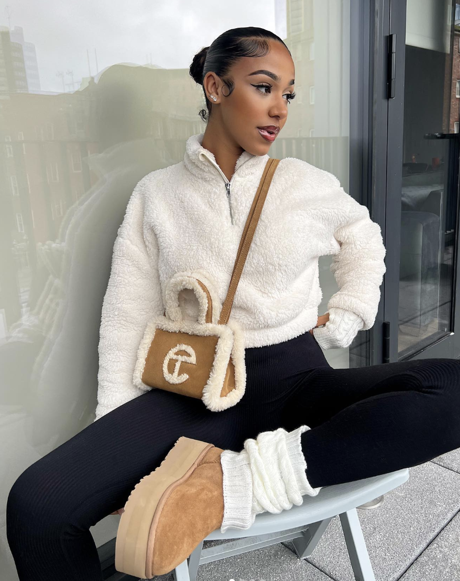 Cream half-zip fleece and black leggings with white socks, chestnut ankle boots and a small textured bag.