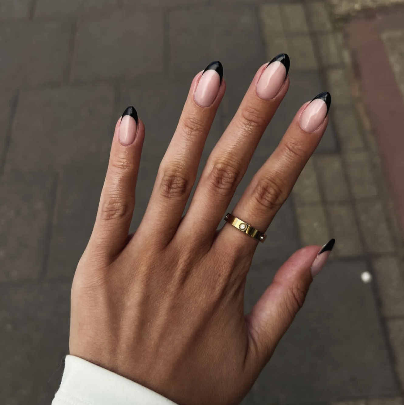 Long almond-shaped nails with a glossy nude base and a sleek, deep black French tip.