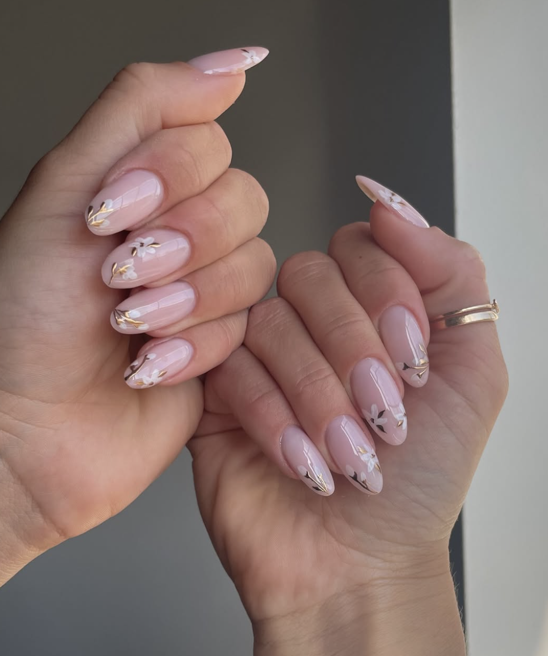 Almond-shaped milky white nails with hand-painted white floral outlines and gold foil accent